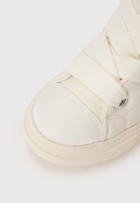 Cremefarbene Leder-Sneaker mit texturierten Stoffschnürsenkeln, abgerundetem Zehenbereich und Gummisohle, die ein dezentes Profildesign für besseren Halt aufweist.