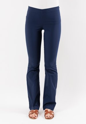 Pantaloni attillati di colore blu navy, realizzati in tessuto elastico con fondo svasato. Presentano una vita elasticizzata. Indossati con sandali marroni con cinturini.