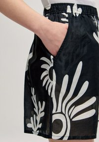 Jupe en tissu noir avec des motifs floraux abstraits blancs, taille élastique, poches latérales et une texture légère et respirante.