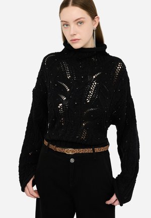 Maglione nero lavorato a maglia con un intricato design a traforo e dettagli di perline, abbinato a pantaloni neri e una cintura con stampa leopardata.
