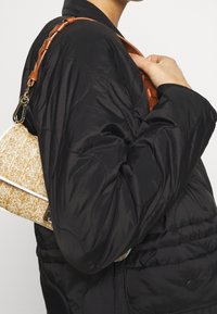 Fodrad svart jacka bärs med en kräm- och beige vävd handväska med läderrem och guldfärgad detaljer.