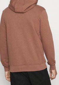 Felpa con cappuccio di colore rosa polveroso, realizzata in un tessuto morbido, con maniche lunghe e tasca a marsupio. Design semplice con cappuccio regolabile.