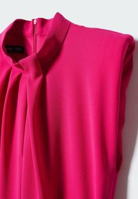 Robe rose vif avec col montant, détail froncé sur le devant et fermeture éclair visible dans le dos, posée à plat sur une surface blanche.