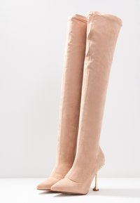 Knä-höga, blush mockaläder stövlar med spetsiga tår och stiletto-hälar. Har guldtonad hårdvara och pärlanknytningar på hälen.