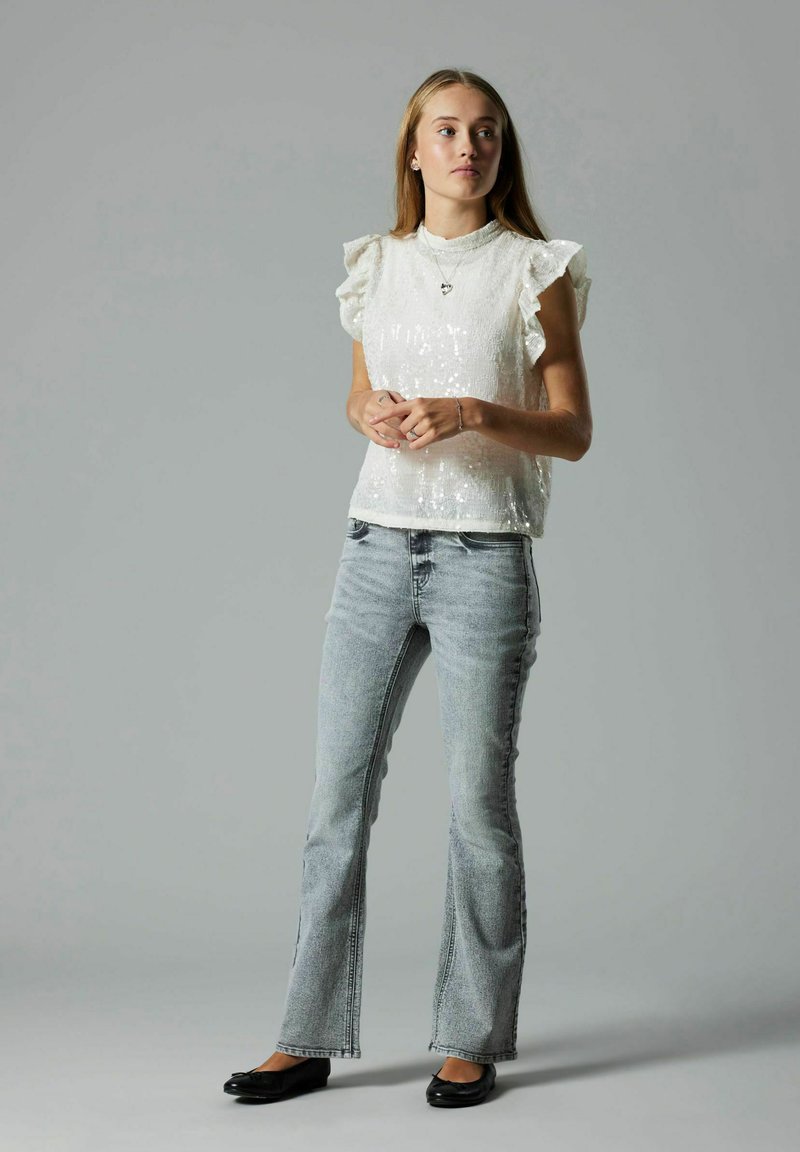 Valge sädelev pluus volangitega varrukatel, koos helesiniste laienevate teksade ja mustade korteritega. Lihtne disain pehme tekstuuriga.