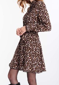 Robe florale marron avec un corsage ajusté, des manches longues et un ourlet évasé. Agrémentée de petits motifs floraux colorés et d'un tissu texturé.