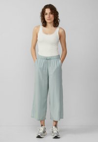 Helle blaue, weit geschnittene Hose mit lockerer Passform und elastischem Bund, kombiniert mit einem weißen Tanktop und silbernen Sneakers.