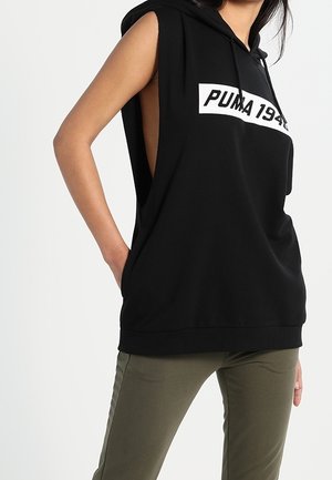 Czarna bezrękawnikowa bluza Puma z dużymi otworami na ramiona i białym logo "PUMA 1948", noszona z oliwkowozielonymi spodniami.