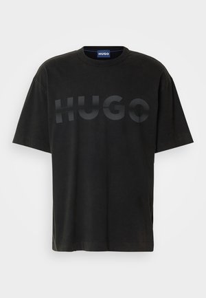 Μαύρο βαμβακερό t-shirt με στρογγυλή λαιμόκοψη και κοντά μανίκια. Διαθέτει έναν μεγάλο, ανάγλυφο λογότυπο "HUGO" σε τονική σχεδίαση στο στέρνο.