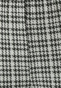 Tkanina sa uzorkom houndstooth u crnoj i bijeloj boji, s teksturiranim tkanjem, oštrim kutovima i kontrastnim bojama.