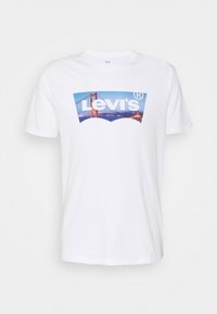 Valkoinen puuvillapaita, jossa on sininen Levi's-logo ja kuva Golden Gate -sillasta. Lyhyet hihat, pyöreä pääntie.