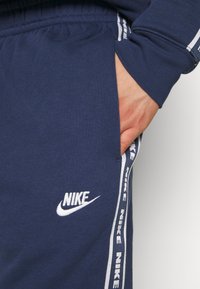 Tums zils kokvilnas džemperi ar baltu Nike logo un sānu svītrām. Iezīmes: elastīgs jostasvērts un rokas kabata. Mīksta tekstūra, ikdienišķs dizains.