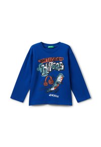 T-shirt à manches longues bleue en coton, ornée d'une impression graphique avec un skate et des écouteurs. Le texte indique "N'ÉCOUTEZ PAS LES CRITIQUES."