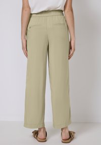 Licht olijfgroene wijde broek met een elastische tailleband en achterzakken. De stof lijkt glad met een licht glanzende textuur.