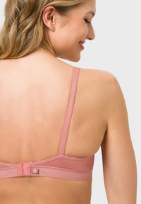 Rosa BH mit verstellbaren Trägern, Haken- und Ösenverschluss auf der Rückseite, glattem Stoff und subtilen Logodetails am Bund. Hat ein minimalistisches Design.