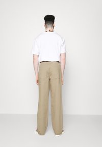 Béžové kalhoty s širokými nohavicemi a zadními kapsami, spárované s bílým tričkem s krátkým rukávem. Tento outfit je minimalistický a neformální.