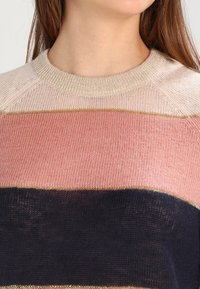 Gebreide trui met horizontale strepen in zachtroze, beige en marineblauw, met metallic gouden accenten langs de randen en de halslijn.