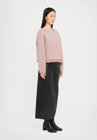 Maglione rosa corto con orlo arricciato, maniche lunghe, abbinato a una gonna maxi nera in pelle aderente e stivali neri con tacco fino al polpaccio.