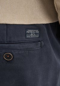 Pantalon en coton bleu marine avec une texture diagonale subtile, doté d'un bouton marron et d'une étiquette de Petrol Industries sur la poche arrière.