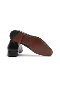 Chaussures habillées en cuir noir avec une finition lisse, comportant des perforations décoratives, un petit talon, et une semelle en cuir brun avec une marque imprimée.