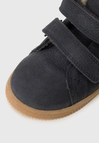 Čierna kožená topánka so semišovou textúrou, ktorá má dva suché zipsy a gumenú podrážku. Tvar je zaoblený, vhodný na každodenné nosenie.