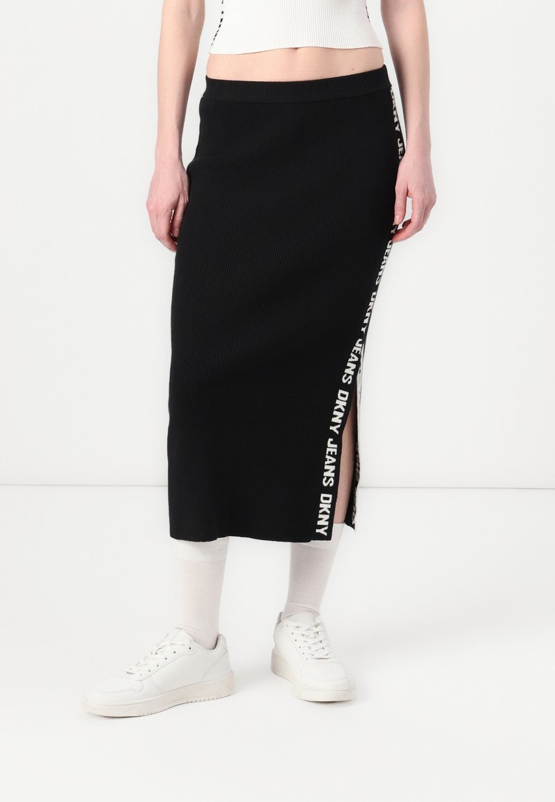 Melna ribota midi svārki ar sānu izgriezumu un ar logo apdari "DKNY JEANS" gar malu. Apvienoti ar baltām sporta apaviem.