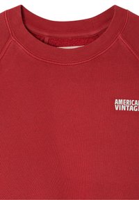 Raudona megztinė su apykakle, raukinėtos rankovės ir apačia, minkštas audinys, prie krūtinės yra balta "AMERICAN VINTAGE" tekstinė logo.