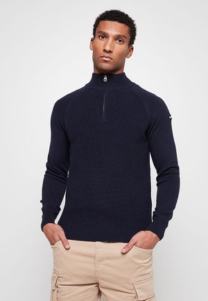 Pull-over côtelé bleu marine avec col montant à fermeture éclair et manches longues ; tissu en maille texturée, coupe ajustée.