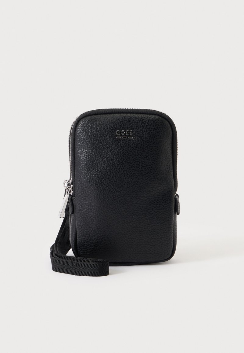 Sac bandoulière en cuir noir texturé avec une fermeture éclair argentée et un logo "BOSS" sur le devant, présenté sur un fond clair uni.