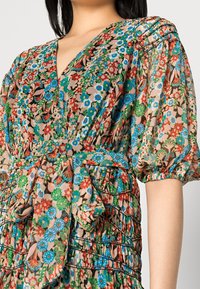 Blommig klänning med puffärmar i livliga blå, gröna, röda och rosa mönster. Har en djup V-ringning och ett knytbart midjeband med plisserade detaljer.