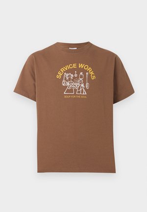 T-shirt marron avec texte jaune « SERVICE WORKS » et « SOUP FOR THE SOUL », avec un dessin au trait blanc de deux personnes partageant de la nourriture et des ustensiles de cuisine suspendus.