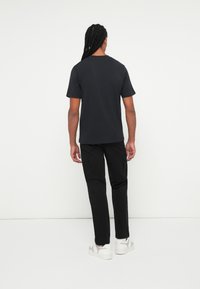 Tricou scurt negru cu guler rotund, asortat cu pantaloni cargo negri și adidași albi, văzut din spate. Textură de țesătură netedă.