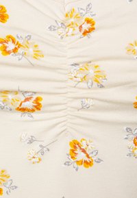 Tecido floral com um fundo creme, apresentando flores amarelas e laranjas. O material é texturizado com detalhes franzidos ao longo das costuras.