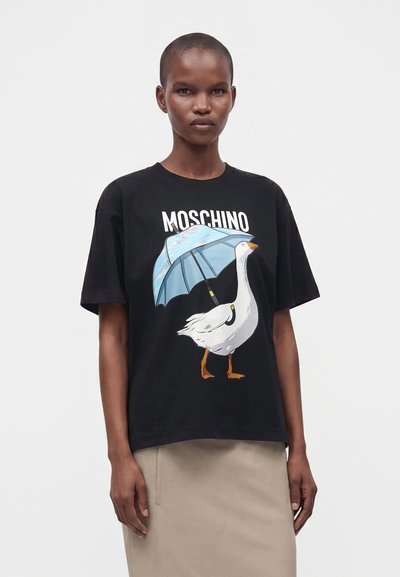 Άτομο που φοράει μαύρο t-shirt Moschino με λευκή χήνα που κρατάει μια μπλε ομπρέλα και μπεζ φούστα.