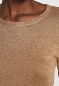 Maglione lavorato a maglia marrone chiaro con scollo rotondo e bordi a coste, caratterizzato da una trama liscia e una forma attillata.