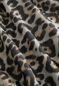 Tekstila s uzorkom leoparda koja prikazuje crne točke na tamnoj pozadini s teksturiranom površinom. Tkanina izgleda mekano i blago prozirno.