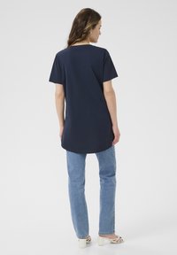 T-shirt en coton bleu marine avec un ourlet rond et des manches courtes, associé à un jean bleu clair et des sandales à talons blocs blanches.