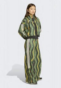 Tepláková súprava s zelenými a žltými zigzagovými vzormi, čiernymi akcentmi a bielymi pruhmi. Materiál pôsobí ľahko a mierne lesklo.