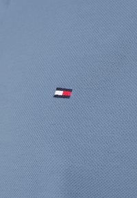 Himmelsblå polo shirt med en texturerad tyg. Har en liten broderad logotyp i röd, vit och blå som är placerad på vänster bröst.