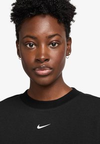Zwarte sweatshirt met ronde hals en korte mouwen, voorzien van een klein wit Nike-logo op de borst. Glad materiaal, aansluitend ontwerp.