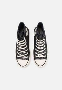 Zwarte high-top sneakers met een getextureerde glanzende afwerking, witte veters, rubberen neuskap en een logo patch aan de zijkant.