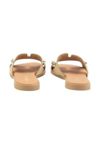 Sandalias planas con un upper de ante beige, parte trasera abierta, acentos metálicos decorativos y una plantilla suave en tono bronceado. Diseño simple con hardware mínimo.