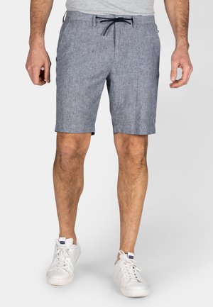 Blauwe gestreepte shorts van een lichtgewicht stof met een trekkoordsluiting. Heeft zijzakken en valt boven de knie. Gdragen met witte sneakers.