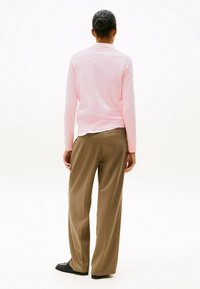Felpa rosa realizzata in un tessuto morbido, abbinata a pantaloni brown a vita alta e bucolici. Una camicia bianca è indossata sotto la felpa.