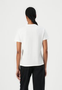 White short-sleeve t-shirt with a crew neck, smooth texture, fitted design, and double-stitched hem, paired with black denim pants.