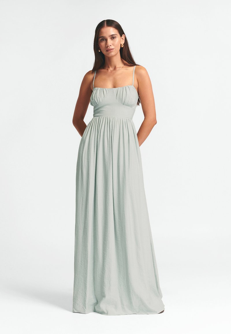 Šviesiai žalia maksi suknelė su plonais petnešomis, susikaupusiu liemeniu ir laisvai krintančia sijonine dalimi. Pagaminta iš tekstūruotos medžiagos, turi laisvą kirpimą.