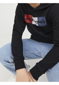 Felpa nera con polsini a coste, presenta una grafica a strisce nei colori rosso, bianco e blu con il testo "JACK & JONES" sulla parte anteriore.