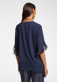 Blusa blu navy con maniche trasparenti a volants e vestibilità comoda. Caratterizzata da un orlo dritto e un tessuto morbido e leggero.