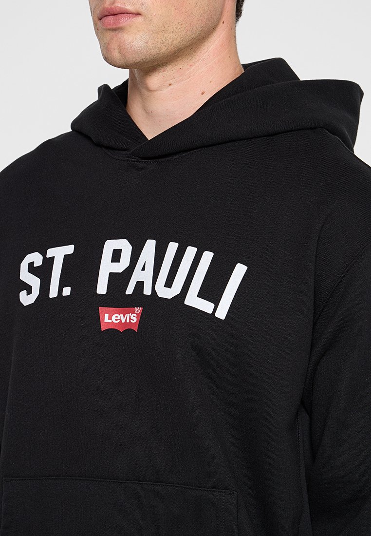 Schwarzer Hoodie mit "ST. PAULI" in weißer Schrift und rotem Levi's-Logo. Weicher Stoff mit einer Fronttasche und einer Kordelzugkapuze.