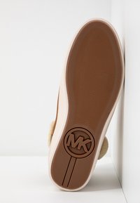 Semelle extérieure en caoutchouc marron avec un grip texturé, dessus fuzzy beige, et logo MK embossé au centre de la semelle, présenté sur un fond blanc.